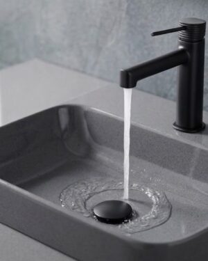 Misturadora monocomando de lavatório série Firenze IMEX em acabamento preto mate instalada num lavatório cinzento.
