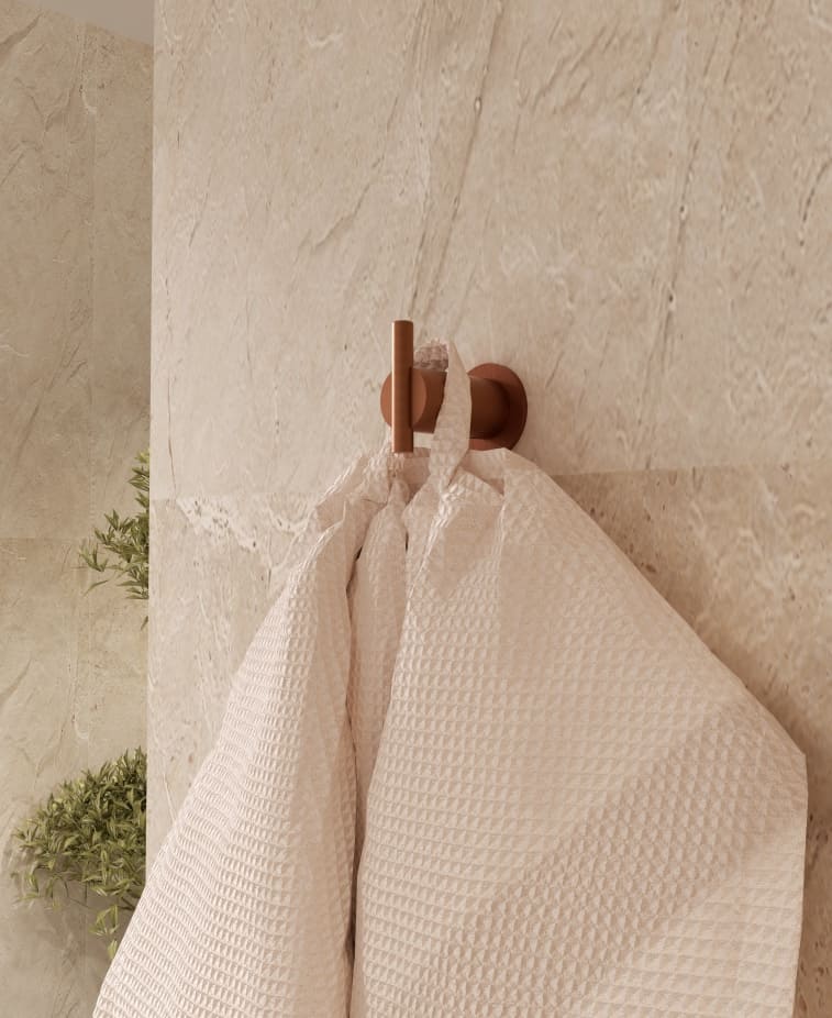 Cabide para casa de banho Imex Série Time em ouro rosa escovado instalado na parede com toalha de banho.